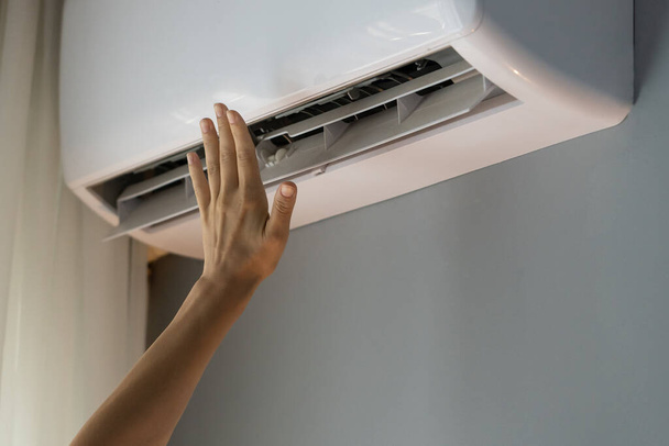 Female owner of apartment stretches hand to check operating air conditioner and catch stream of warm air. Person wants to make flat warm turning on modern device. Landlady enjoys caring about house - Photo, Image