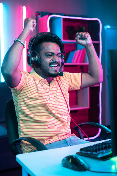 vertical shot of Cheerful gamer celebrating win by raising hands while playing online video game at home - concept of achievement, champion and successful - Photo, Image