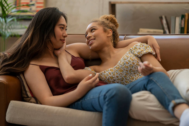 2人の多人種の若いレズビアン女性が自宅のソファで - 写真・画像