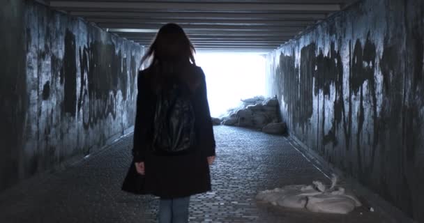 Silhouette donna cammina lungo un passaggio sotterraneo trasformato in un rifugio antiatomico verso la luce. Vista posteriore, tunnel squallido, sacchi di sabbia. Guerra in Ucraina. Filmati 4k di alta qualità - Filmati, video