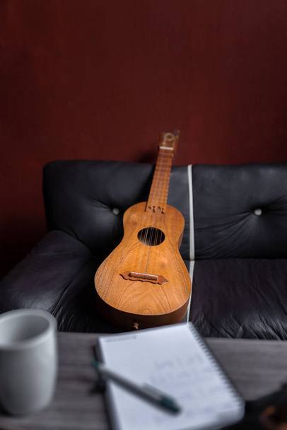 Een Mexicaanse jarana gitaar rust op een bank achter een notebook. Concept van het componeren van muziek thuis - Foto, afbeelding
