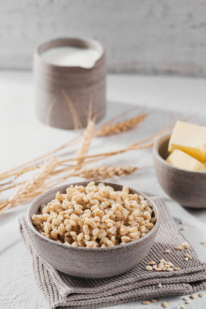 Bowl of cooked peeled barley grains porridge with ears of wheat on white background. Cooking Healthy and diet food concept. - 写真・画像
