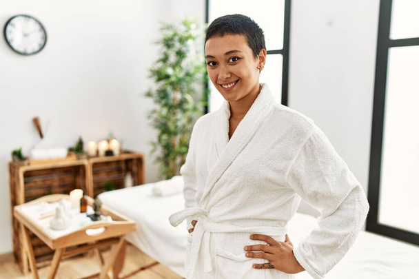 Young hispanic woman wearing bathrobe smiling confident at beauty center - 写真・画像