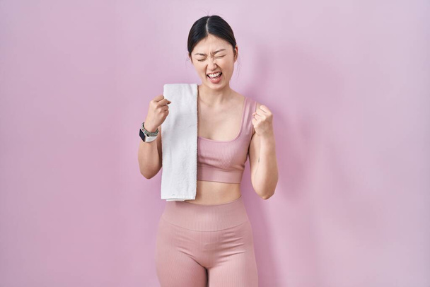 Chińska młoda kobieta ubrana w odzież sportową i ręcznik bardzo szczęśliwy i podekscytowany robi gest zwycięzcy z podniesionymi ramionami, uśmiechnięta i krzycząc o sukces. koncepcja uroczystości.  - Zdjęcie, obraz