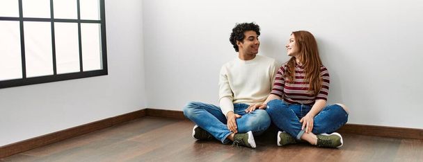 Fiatal spanyol pár mosolyog boldogan ül a padlón egy üres új otthonban.. - Fotó, kép
