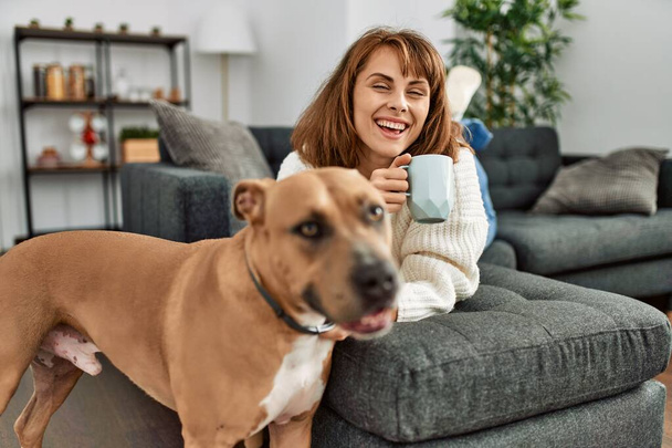 Kafkasyalı bir kadın evdeki köpekle kanepede kahve içiyor. - Fotoğraf, Görsel