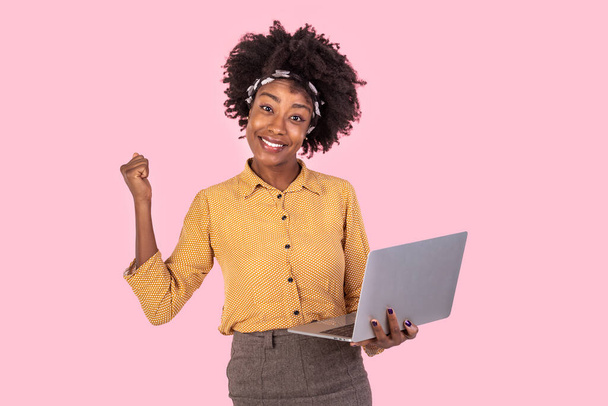 Щаслива афро-американська жінка тримає ноутбук і піднімає руку, щоб відсвяткувати успіх або досягнення. - Фото, зображення