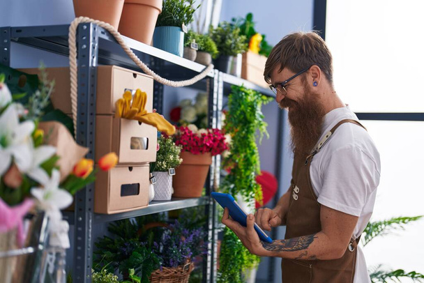 Giovane uomo rossa fiorista sorridente fiducioso utilizzando touchpad al negozio di fiori - Foto, immagini