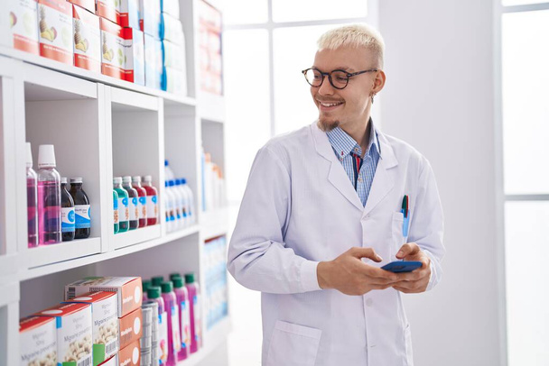 Young caucasian man pharmacist using smartphone working at pharmacy - Photo, Image