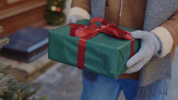 Mans kesztyűben tartja a nagy karácsonyi ajándékot piros szalaggal, miközben a férfi megy. Újévi ünnepség. Közelről. Emberek és karácsonyi ünnepek koncepciója - Felvétel, videó