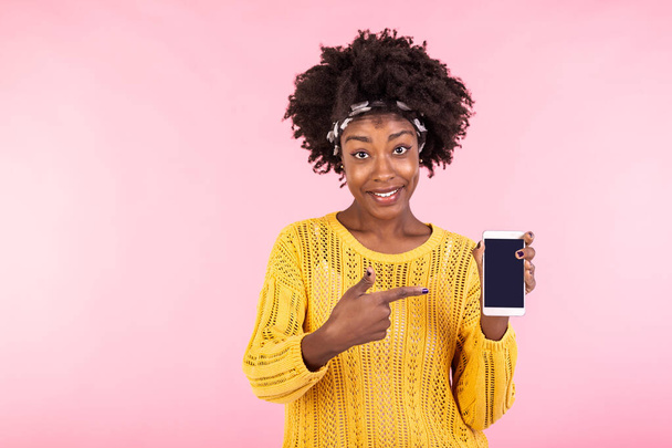 Νεαρή γυναίκα εμφανίζεται στο τηλέφωνο. Αφροαμερικανή γυναίκα χαμογελά και δείχνει το δάχτυλο στο smartphone. Διαφήμιση έννοιας - Φωτογραφία, εικόνα