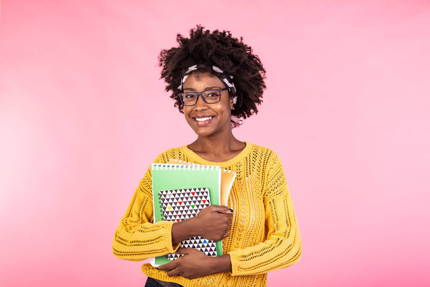 Young female student in glasses holding books in hand isolated on pink background portrait, casual daily lifestyle student holding notebooks smiling - Foto, afbeelding