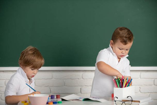 Portret dzieci w szkole przyjemnie odrabiają pracę domową, trzymają ołówek, piszą. Dzieci uczą się rysunku na podstawówce. Kreatywny rozwój dzieci - Zdjęcie, obraz