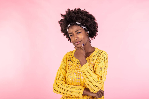 Podejrzana młoda Afrykanka z nieufną twarzą patrząca w kamerę, sceptyczna sarkastyczna czarna dziewczyna czująca się ostrożna, wątpliwa nieufność odizolowana na różowym tle studia - Zdjęcie, obraz