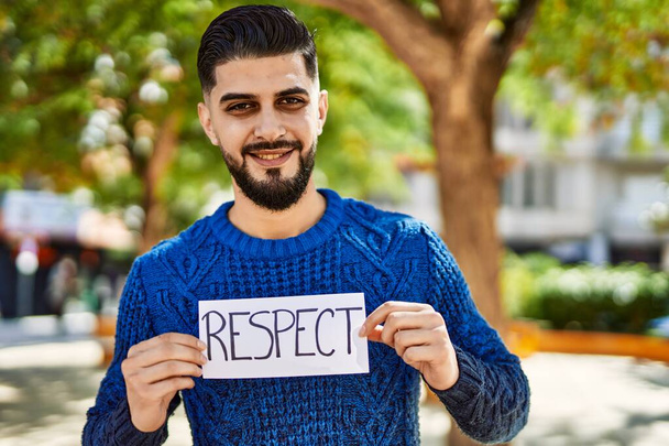 młody arabski człowiek uśmiecha się pewnie trzymając sztandar szacunku w parku - Zdjęcie, obraz