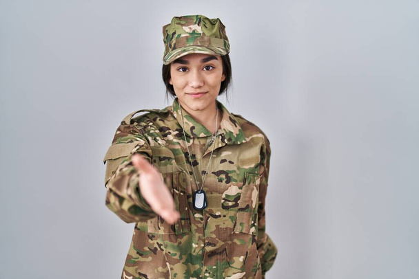 Nuori Etelä-Aasian nainen yllään naamiointi armeijan univormu hymyilevä tarjoten palmu käsi antaa apua ja hyväksyntää.  - Valokuva, kuva