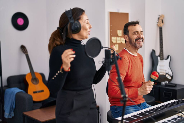 Orta yaşlı erkek ve kadın müzisyenler müzik stüdyosunda piyano çalıp şarkı söylüyorlar. - Fotoğraf, Görsel
