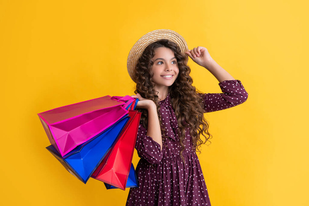 positive kid with curly hair hold shopping bags on yellow background. - Zdjęcie, obraz