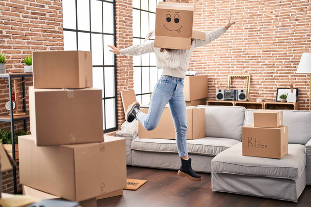 Young woman dancing with funny cardboard box on head at new home - Photo, Image