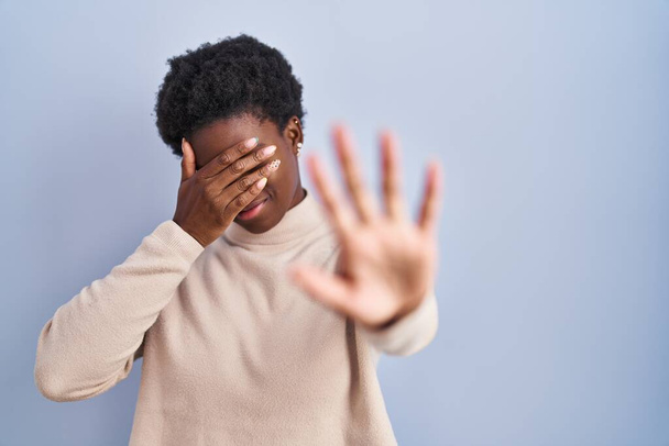 African american woman standing over blue background covering eyes with hands and doing stop gesture with sad and fear expression. embarrassed and negative concept.  - Foto, afbeelding