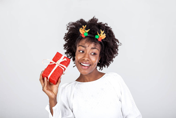 Ενθουσιασμένη μαύρη γυναίκα που τρέμει τυλιγμένο κουτί δώρου που λαμβάνει δώρα για τα γενέθλιά της ή τα Χριστούγεννα στέκεται πάνω από λευκό φόντο. Στιγμιότυπο - Φωτογραφία, εικόνα