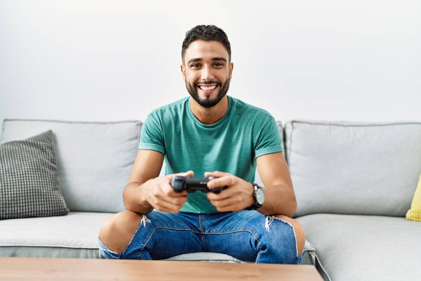 Mladý arabský muž hraje videohry sedí na pohovce doma - Fotografie, Obrázek