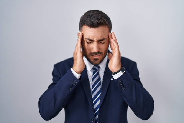 Hombre hispano guapo usando traje y corbata con la mano en la cabeza, dolor de cabeza porque el estrés. padecer migraña.  - Foto, imagen