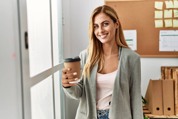 Fiatal kaukázusi üzletasszony kávézik az ablak előtt az irodában. - Fotó, kép