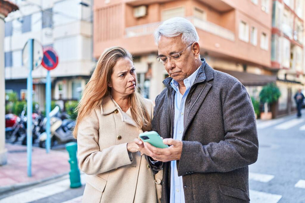 Hombre y mujer de mediana edad utilizando el teléfono inteligente en la calle - Foto, Imagen