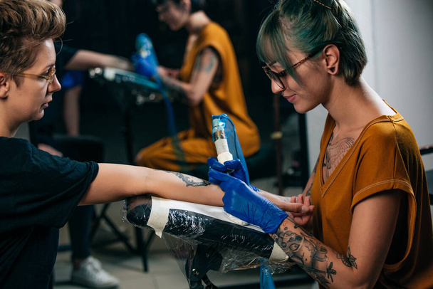 Primo piano tatuatore dimostra il processo di ottenere tatuaggio nero con vernice. Master lavora con guanti sterili blu. Maestro del tatuaggio del circuito di riempimento del tatuaggio. - Foto, immagini