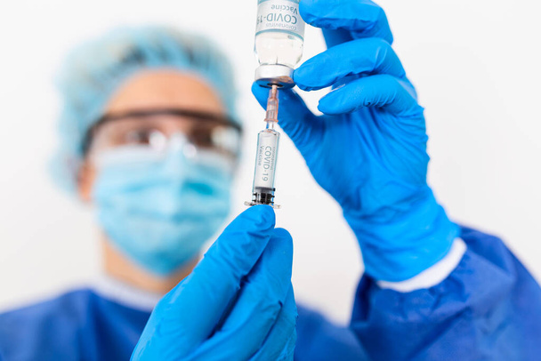Nahaufnahme Hand einer Ärztin oder Wissenschaftlerin in PSA-Uniform mit Mundschutz im Labor halten Medizin Flüssigkeit Impfflasche und Spritze, Coronavirus oder COVID-19 Konzept weiß isoliert - Foto, Bild