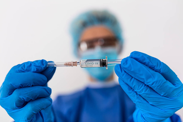 Epidemia chińskiego koronawirusa. Lekarz w kombinezonie ochronnym i masce posiada strzykawkę i szczepionkę. Szczepionka przeciw grypie, koronawirusowi - Zdjęcie, obraz