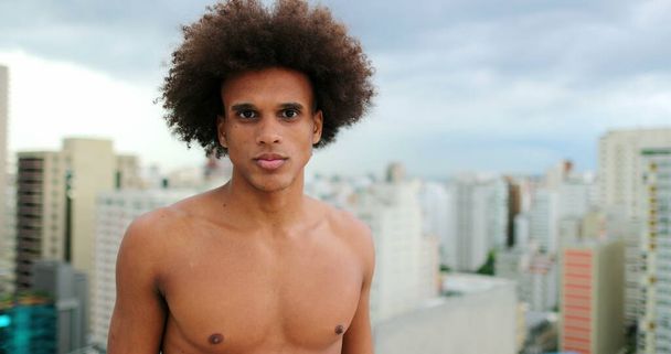 Shirtless young handsome mixed race african man standing on top of rooftop - 写真・画像