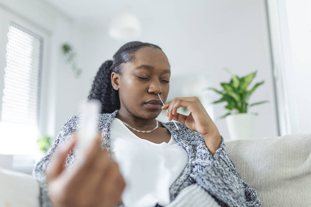 Nuori afrikkalainen nainen, jolla on itsetestaava itsetestaava pyyhkäisynäyte ja lääketieteellinen putki Coronavirus covid-19: lle, ennen kuin se testataan itse kotona - Valokuva, kuva