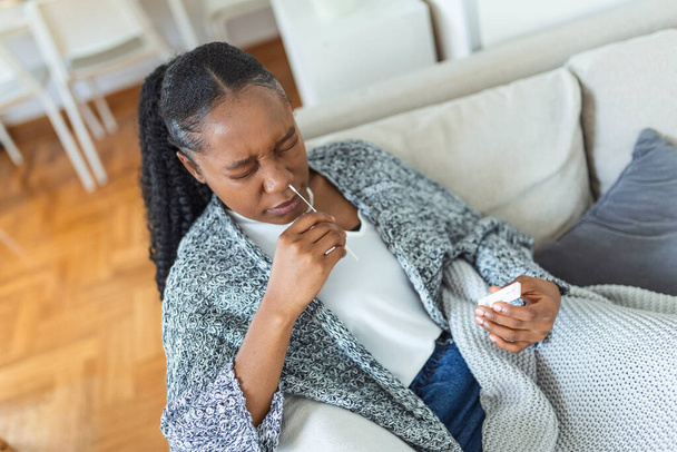 Афро-американка использует ватный тампон во время анализа коронавируса у себя дома. Женщина, использующая коронавирус быстрый диагностический тест. Молодая женщина дома использует мазок из носа для COVID-19. - Фото, изображение