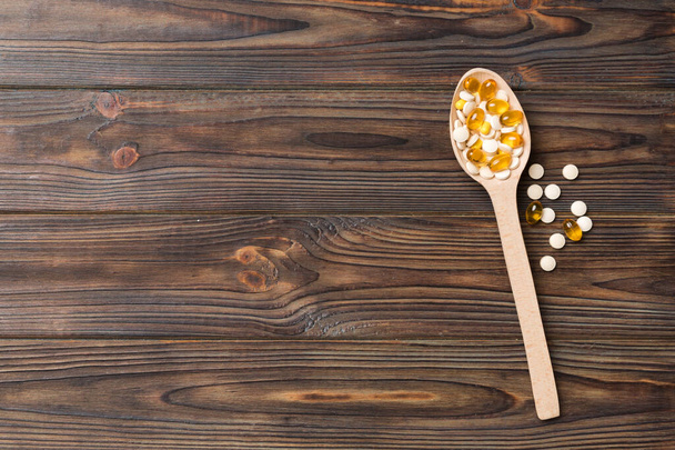 Vitamin capsules in a wooden spoon on a colored background. Pills served as a healthy meal. Drugs, pharmacy, medicine or medical healthycare concept. - Foto, Imagen