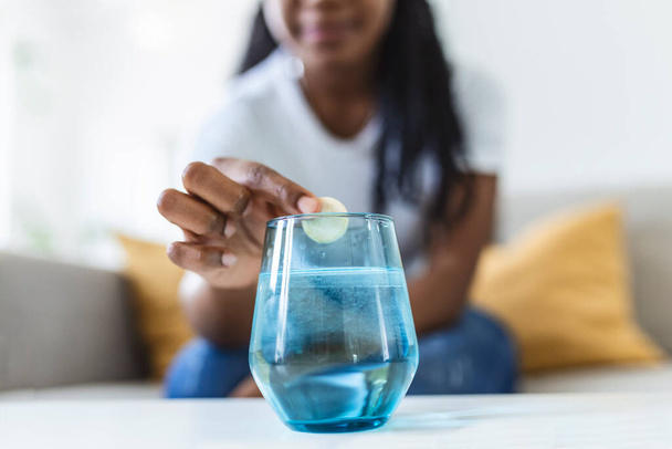Closeup of a young woman dropping an effervescent antacid in a glass of water. young woman hardly put a soluble pill with a medicine for pain or a hangover in a glass of water - Photo, Image