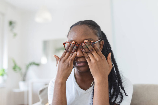 Menina africana em óculos esfrega os olhos, sofrendo de olhos cansados, conceito de doenças oculares
 - Foto, Imagem