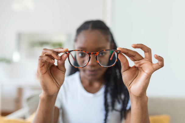 young African woman holds glasses with diopter lenses and looks through them, the problem of myopia, vision correction - Фото, изображение