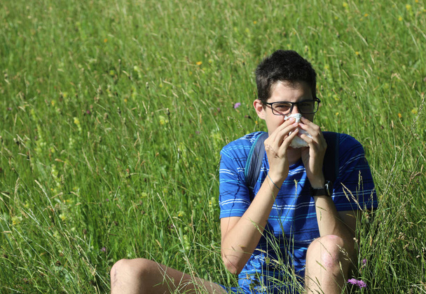 mladý chlapec s brýlemi fouká do nosu kvůli alergii na louce na jaře - Fotografie, Obrázek