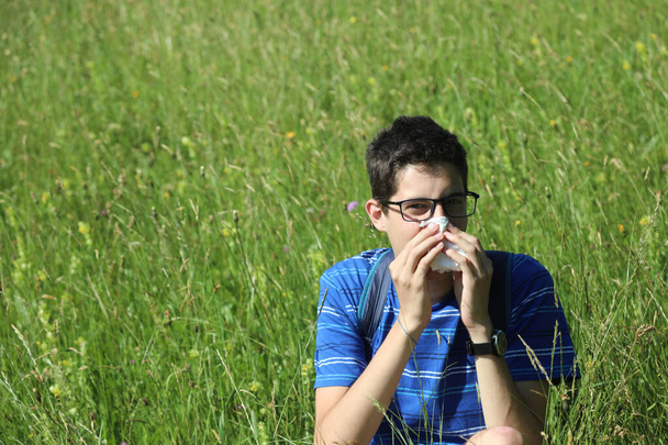 jeune garçon avec des lunettes se mouchant à cause d'une allergie dans la prairie au printemps - Photo, image