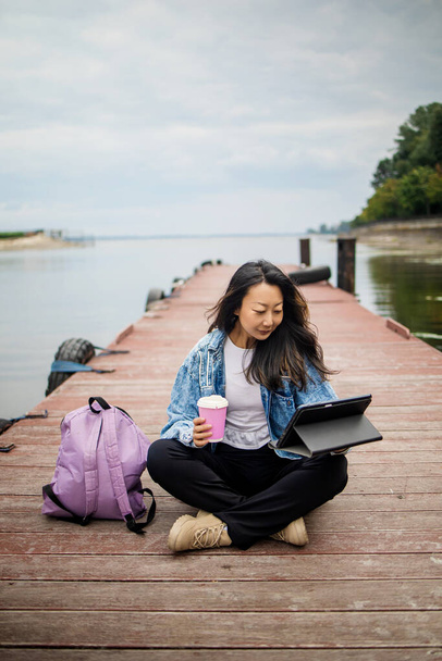 Красива дівчина-мандрівник, яка використовує планшет у дерев'яному мосту. молода дівчина турист з ноутбуком сидить в порту
. - Фото, зображення