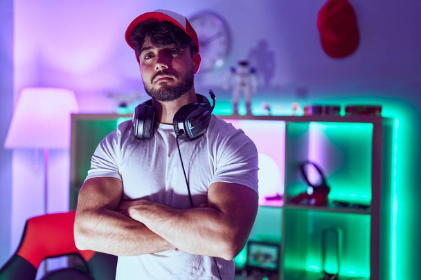 Young hispanic man streamer standing with arms crossed gesture at gamin room - Foto, afbeelding