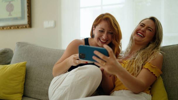 Twee vrouwen drinken koffie kijken video op smartphone thuis - Foto, afbeelding