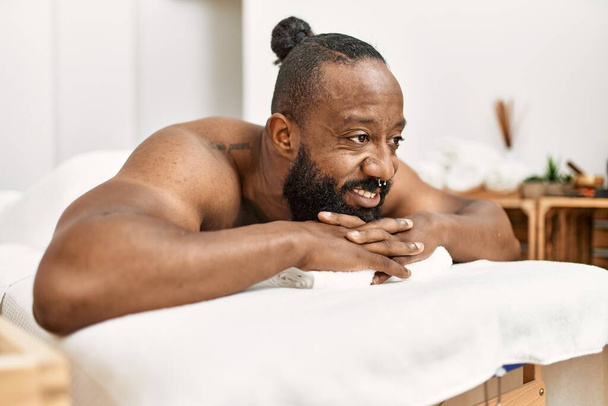 jong afrikaans amerikaans man glimlachen vertrouwen liggend op massage tafel bij beauty center - Foto, afbeelding