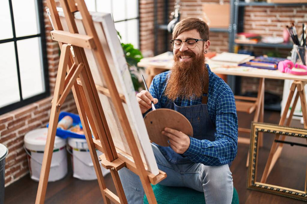 Nuori punapää mies taiteilija hymyilee luottavainen piirustus art studio - Valokuva, kuva