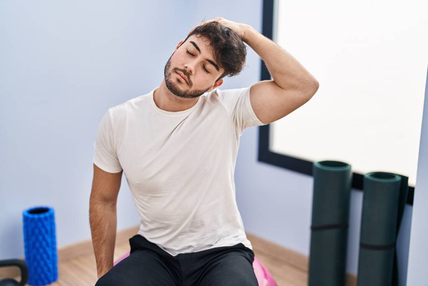 Young hispanic man sitting on fit ball stretching at sport center - Valokuva, kuva