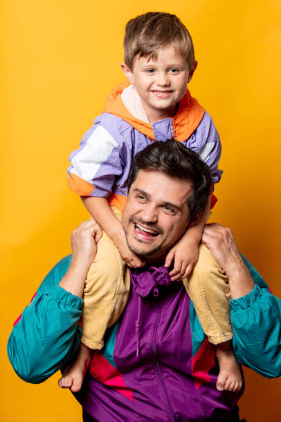 Father with son in 80s vintage sport suits on yellow background  - Photo, Image