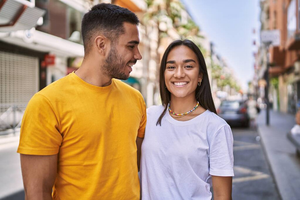 Joven pareja latina sonriendo feliz y abrazándose de pie en la ciudad. - Foto, imagen