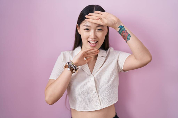 Chinese young woman standing over pink background smiling cheerful playing peek a boo with hands showing face. surprised and exited  - Photo, Image